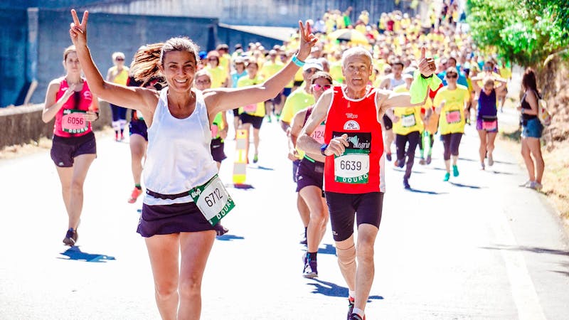 Smiling runners with race bibs taking part in a sunny outdoor community run on a road